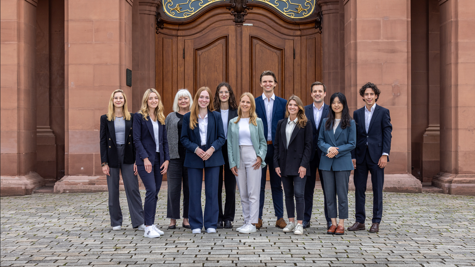 ALle Mitarbeiterinnen und Mitarbeiter des Lehrstuhls stehen aufgereiht vor dem Schloss für ein Teamfoto