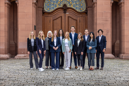 ALle Mitarbeiterinnen und Mitarbeiter des Lehrstuhls stehen aufgereiht vor dem Schloss für ein Teamfoto