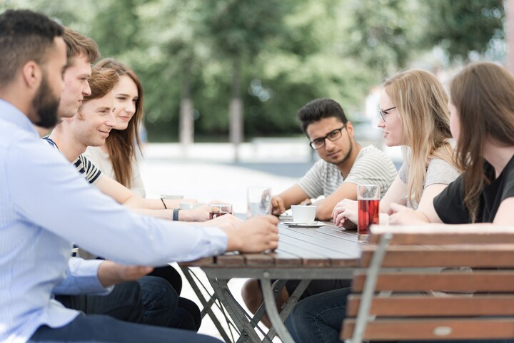 Studierende sitzen um Tisch im Freien mit Getränken