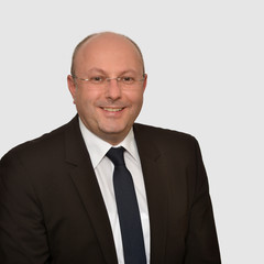 Prof. Stolletz hat eine Brille und trägt einen dunklen Anzug mit Krawatte und weißem Hemd.