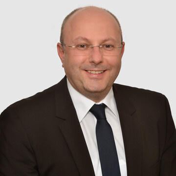 Prof. Stolletz wears glasses and a dark suit with a tie and white shirt.