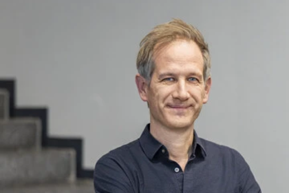 Portrait von Marc Helbling. Er trägt ein dunkelblaues Hemd und hat seine Arme verschränkt.