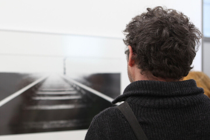 Person von hinten, die auf ein schwarz-weiß Bild von Schienen schaut, das an der Wand hängt
