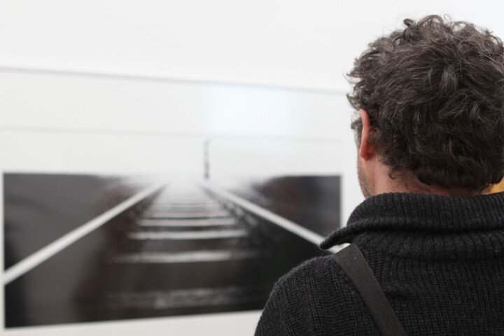 Person von hinten, die auf ein schwarz-weiß Bild von Schienen schaut, das an der Wand hängt