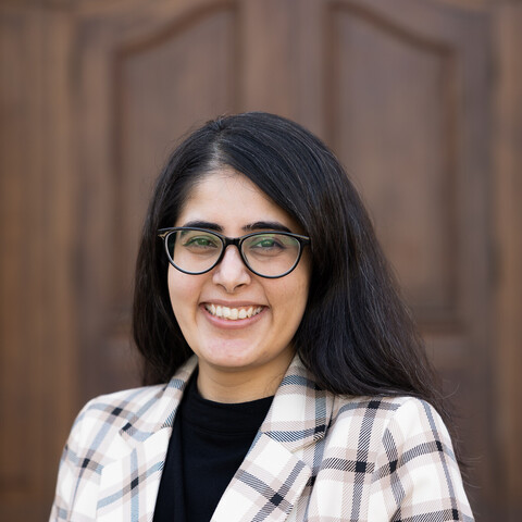 Portait of Himani Singh. She is wearing a white and black checked blazer and is standing in front of a door of Mannheim Palace.
