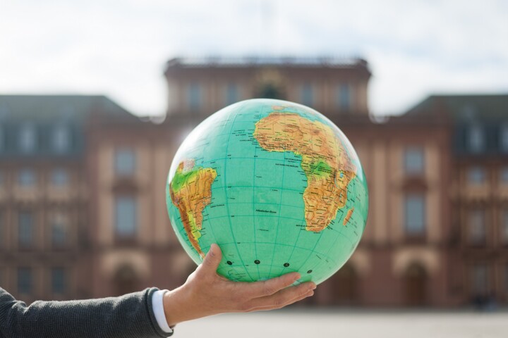 Hand, auf der eine Weltkugel liegt, vor dem Schloss