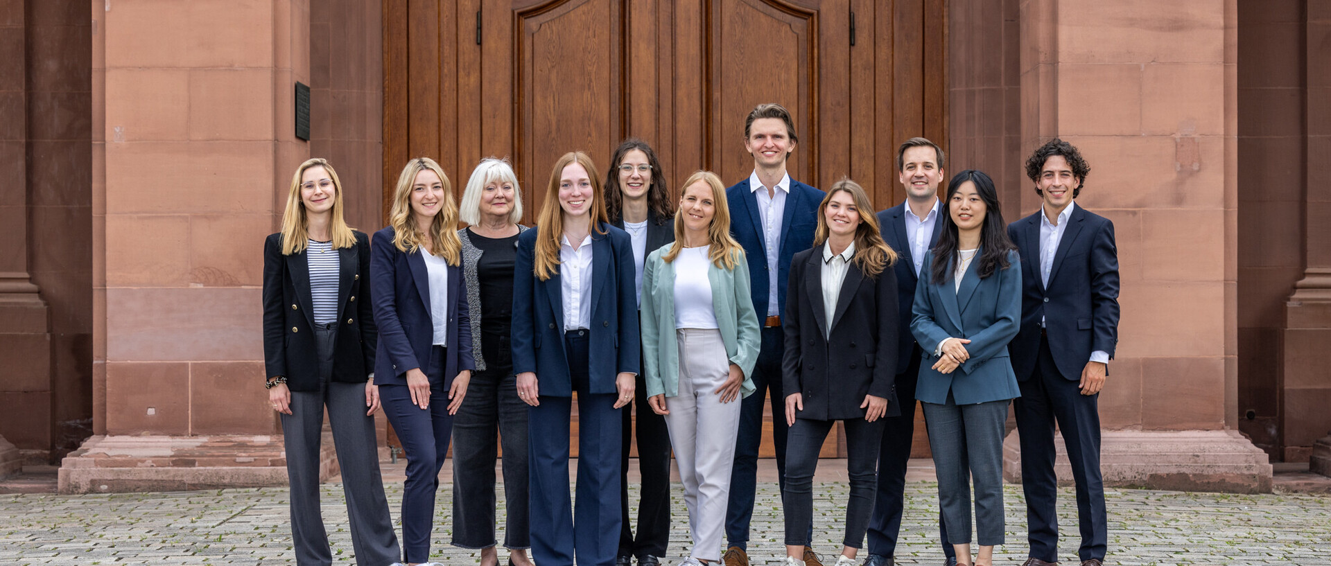 Verschiedene Männer und Frauen im Anzug vor einem Schloss
