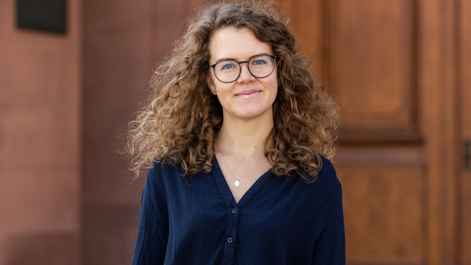 Frau Loetters hat braune lange gelockte Haarre eine Brille und trägt eine blaue Bluse