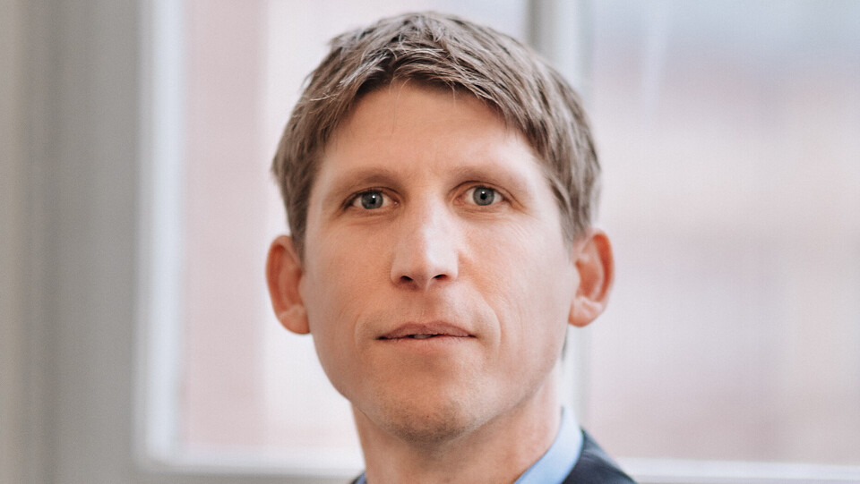 Prof. Biemann hat kurze Haare und trägt ein hellblaues hemd und ein dunkles Jackett. der Hintergrund ist ein Fenster