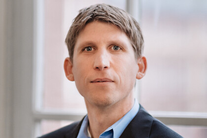 Prof. Biemann hat kurze Haare und trägt ein hellblaues hemd und ein dunkles Jackett. der Hintergrund ist ein Fenster