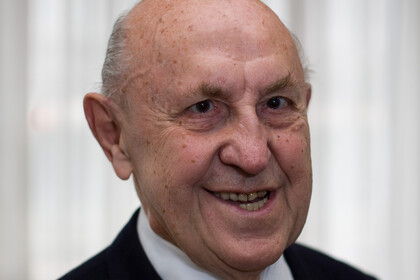 Portrait von Hans Raffee. Er trägt einen schwarzen Blazer mit gelb-braun gepunkteter Krawatte. 