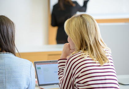 Zwei Studentinnen hören bei einem Vortrag zu.