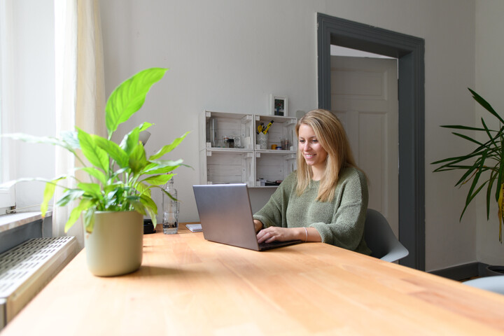 Studierende mit blonden Haaren sitzt in ihrem Zimmer vor ihrem Laptop.