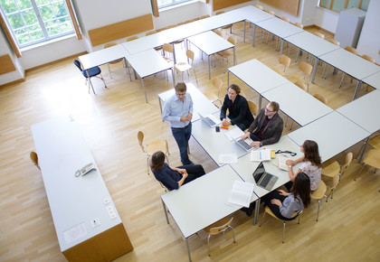 Personen sitzen im Seminarraum um Tische von oben