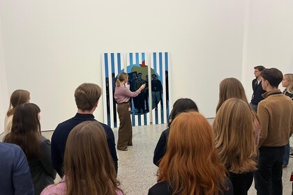 Eine Gruppe von Studenten des Honors Program nimmt an einer Führung durch eine Kunstgalerie teil. Sie hören dem Führer zu und betrachten ein Gemälde.