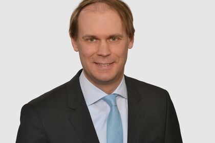Prof. Bischof hat kurze Haare und trägt ein dunkles Jacket, ein helles Hemd und eine türkisfarbene Krawatte.