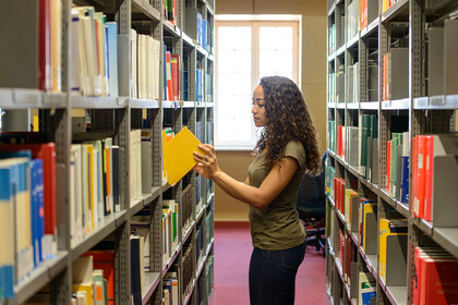 Eine Studentin zieht ein gelbes Buch aus einem Bücherregal in der Bibliothek.