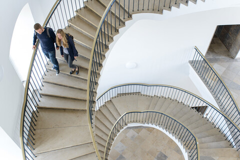 Zwei Studierende laufen eine Wendeltreppe aus Stein in der Uni hinunter