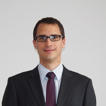 Herr Westerburg hat kurze braune Haare, eine Brille und trägt ein weißes Hemd mit schwarzem Blazer und lila Krawatte