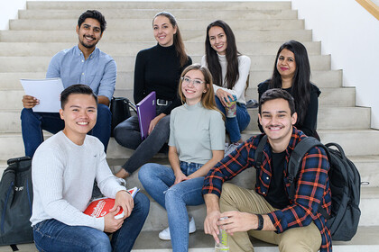Mehrere Studierende sitzen auf einer Treppe. 