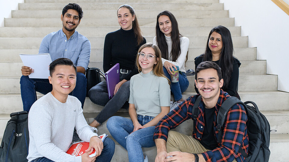Mehrere Studierende sitzen auf einer Treppe.