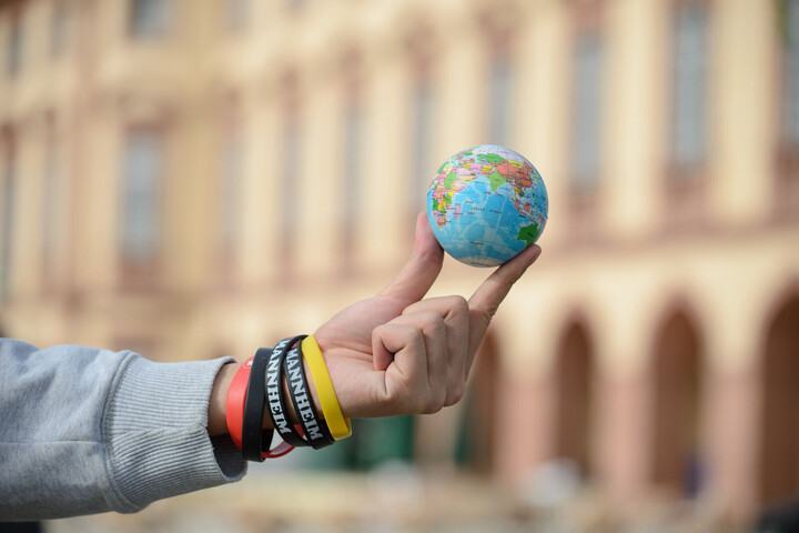 Eine Person hält einen Mini-Globus zwischen den Fingern, mit dem Schloss im Hintergrund.