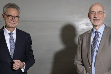 Herr Lutz steht links und trägt eine Brille und einen dunklen Anzug. Herr Puhl steht rechts und trägt eine Brille und einen grauen Anzug