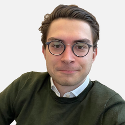 Simon Dimpfl hat kurze braune Haare und eine Brille. Er trägt ein helles Hemd und einen dunklen Pullover. Der Hintergrund ist weiß.