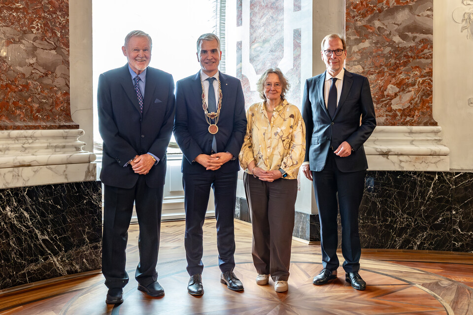 Von links nach rechts: Klaus Greinert, Professor. Dr. Thomas Fetzer, Professor Dr. Rosemarie Tracy und Professor Dr. Jens Wüstemann. Sie stehen auf der Bühne in der Aula und lächeln in die Kamera.