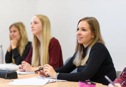 Drei Studentinnen sitzen nebeneinander in einem Seminarraum.