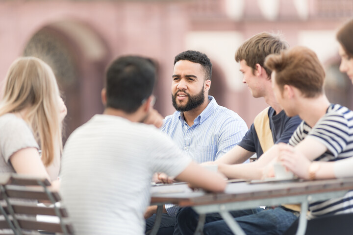 Studierende sitzen im Freien um einen Tisch