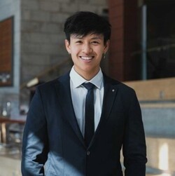 Anh Trinh The has short black hair and wears a dark suit with a white shirt and dark tie