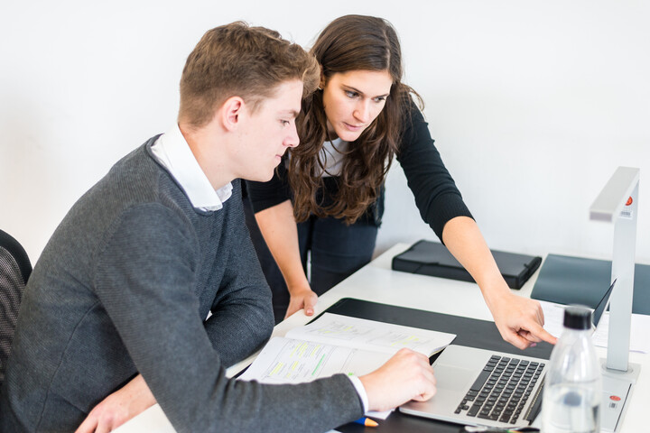 Zwei Personen an Tisch mit Laptop und Arbeitsmaterialien