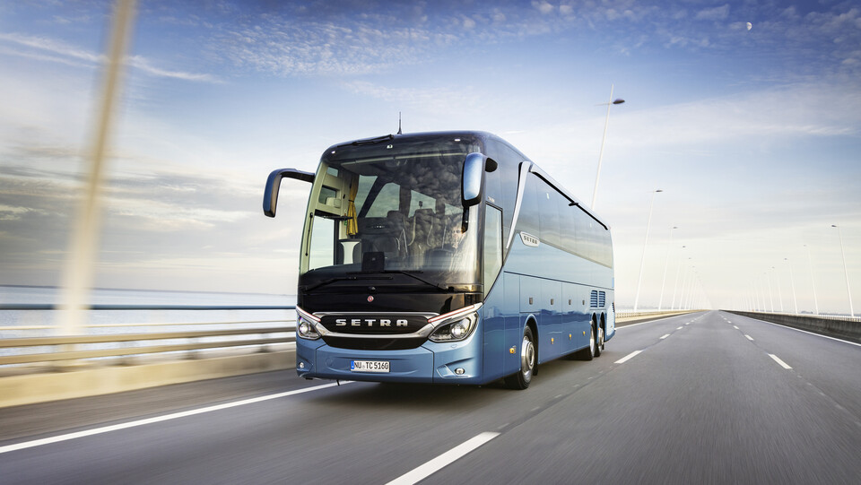 Ein blauer Reisebus fährt über eine Brücke. Im Hintergrund das Meer. 