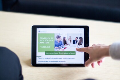 Zoom Tablet Finger zeigt auf Tablet, auf dem steht: Bewerben Sie sich für den Master! Ab 15. März - 31. Mai