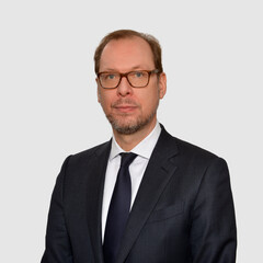 Prof. Wüstemann hat eine Brille und trägt einen dunklen Anzug mit Krawatte.