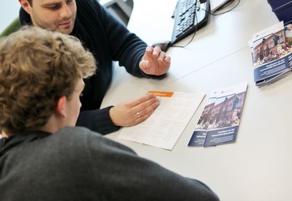 Ein Mitarbeiter berät einen Studenten mit einem Flyer zum Thema "Studieren an der Universität Mannheim".