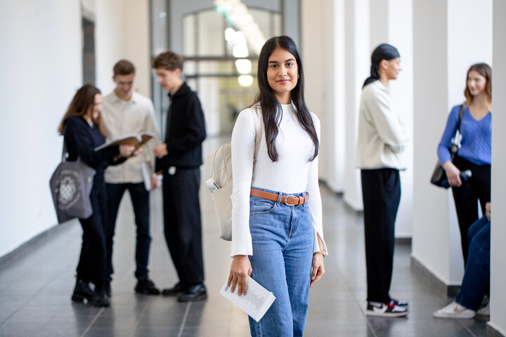 Die Frau auf dem Bild hat lange, glatte schwarze Haare, trägt ein weißes Oberteil und eine Jeans und lächelt in die Kamera