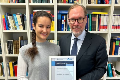 Zwei Personen stehen vor einem Bücherregal und halten eine Urkunde zwischen sich