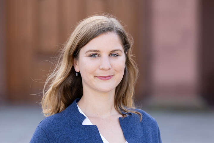 Lea Oberländer außen vor dem Schloss stehend. Sie trägt einen blauen Blazer