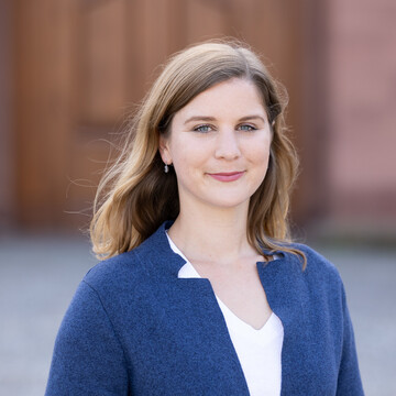 Lea Oberländer has long blonde hair and wears a white blouse and a blue blazer.