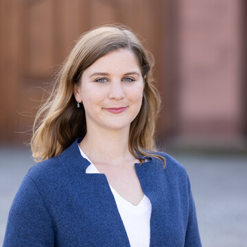 Lea Oberländer has long blonde hair and wears a white blouse and a blue blazer.