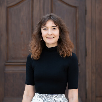 Portrait of Ms. Mueller. She wears a black short-sleeved sweater and stands in front of a door of Mannheim Castle.