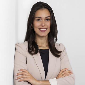 Melany Vogel has long dark hair and is wearing a black top and a light-colored blazer. She has her arms crossed in front of her chest