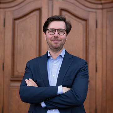 Prof. Dörrenberg hat braunes Haar, trägt eine Brille, ein hellblaues Hemd und einen dunkelblauen Anzug.