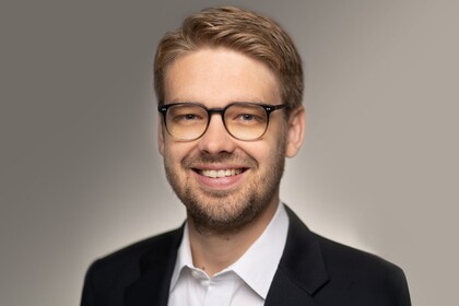 Marc Lerchenmüller hat kurze blonde Haare und eine Brille. Er trägt ein dunkles Jacket und ein weißes Hemd.