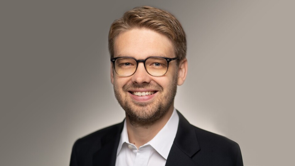 Marc Lerchenmüller hat kurze blonde Haare und eine Brille. Er trägt ein dunkles Jacket und ein weißes Hemd.