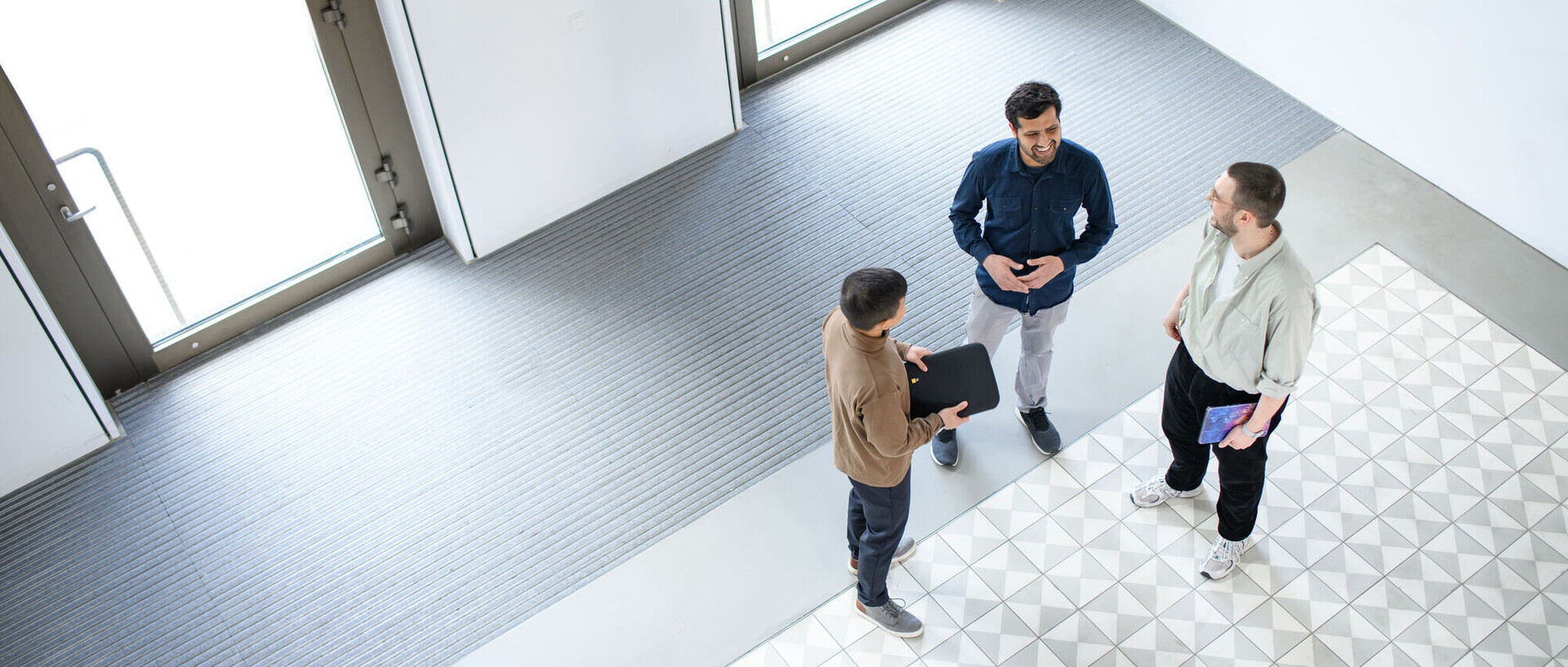 Drei Mitarbeitende der Universität Mannheim stehen im Foyer des B6-Gebäudes und unterhalten sich.