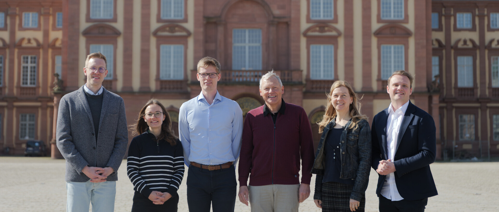 eine Gruppe von sechs Personen steht vor dem Schloss und lächelt in die Kamera