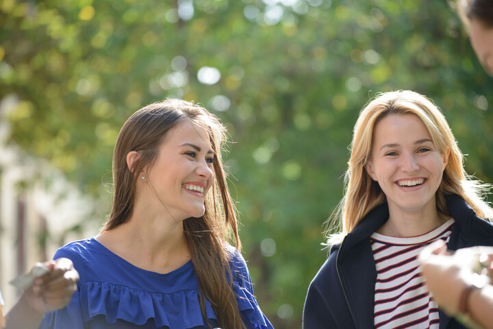 Two students smiling and laughing in front of a green backdrop.